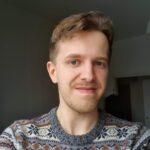 Miesoletettu henkilö, jolla keskiruskeat lyhyet hiukset ja viikset. Henrillä on yllään kuviollinen harmaa neule