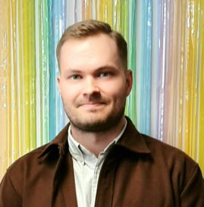 Miesolettu henkilö, jolla on vaalearuskeat lyhyet hiukset ja vaaleat piirteet. Samulilla on tumma lyhyt parta. Päällään Samulilla on vaalea kauluspaita ja ruskea kauluspaita sen päällä.