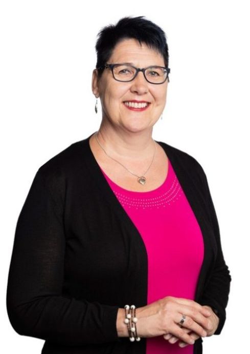 Black-haired smiling woman with dark-rimmed glasses. The woman is wearing a black sweater, with an aniline red t-shirt underneath.