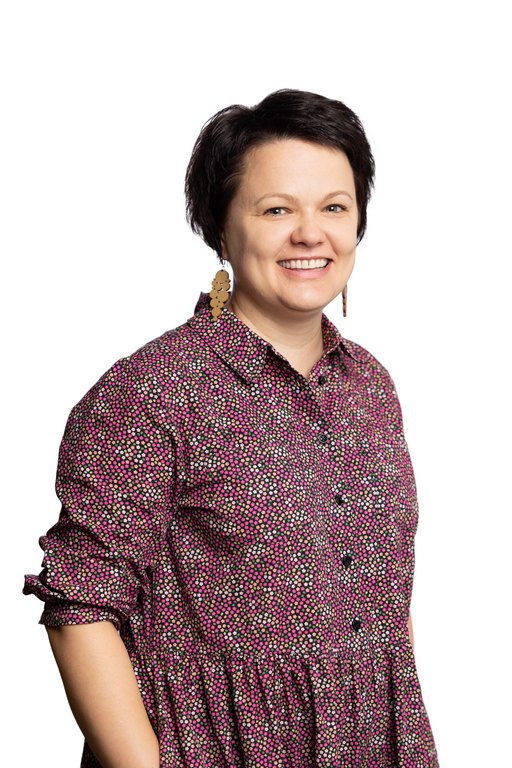 A female presumed person with short dark hair. The person has lång earrings and she smiles happily to the camera. She is wearing a multicolored dress.