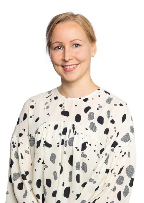 En kvinnlig leende person med blont hår bär en ljus skjorta.