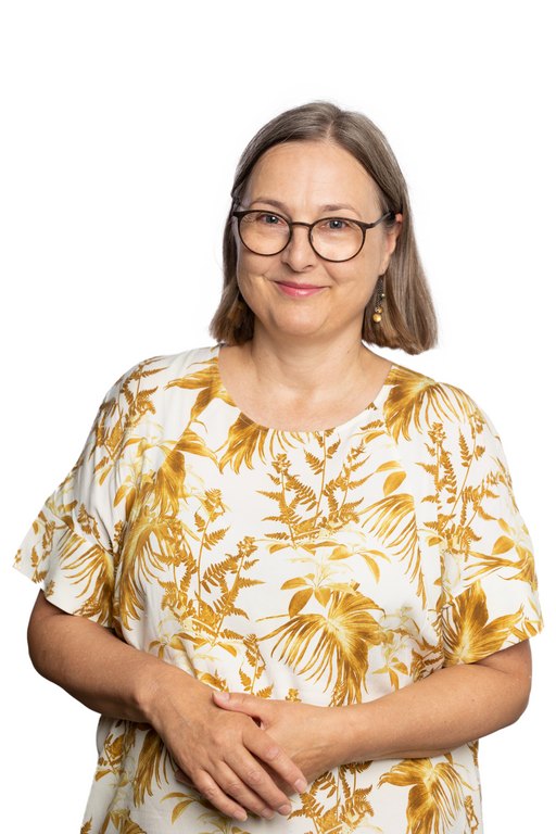 A woman smiles and looks at the camera. She has light brown, semi-long hair and glasses. She is wearing a short-sleeved yellow-white pattern dress.