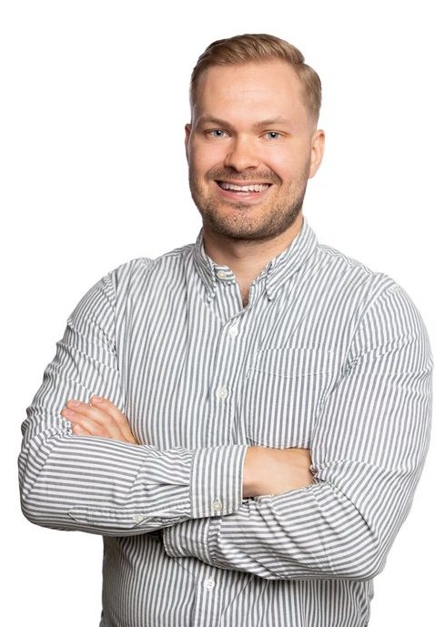 Picture with a man standing in front of a white backround wearing a striped shirt. Smiling to the camera.